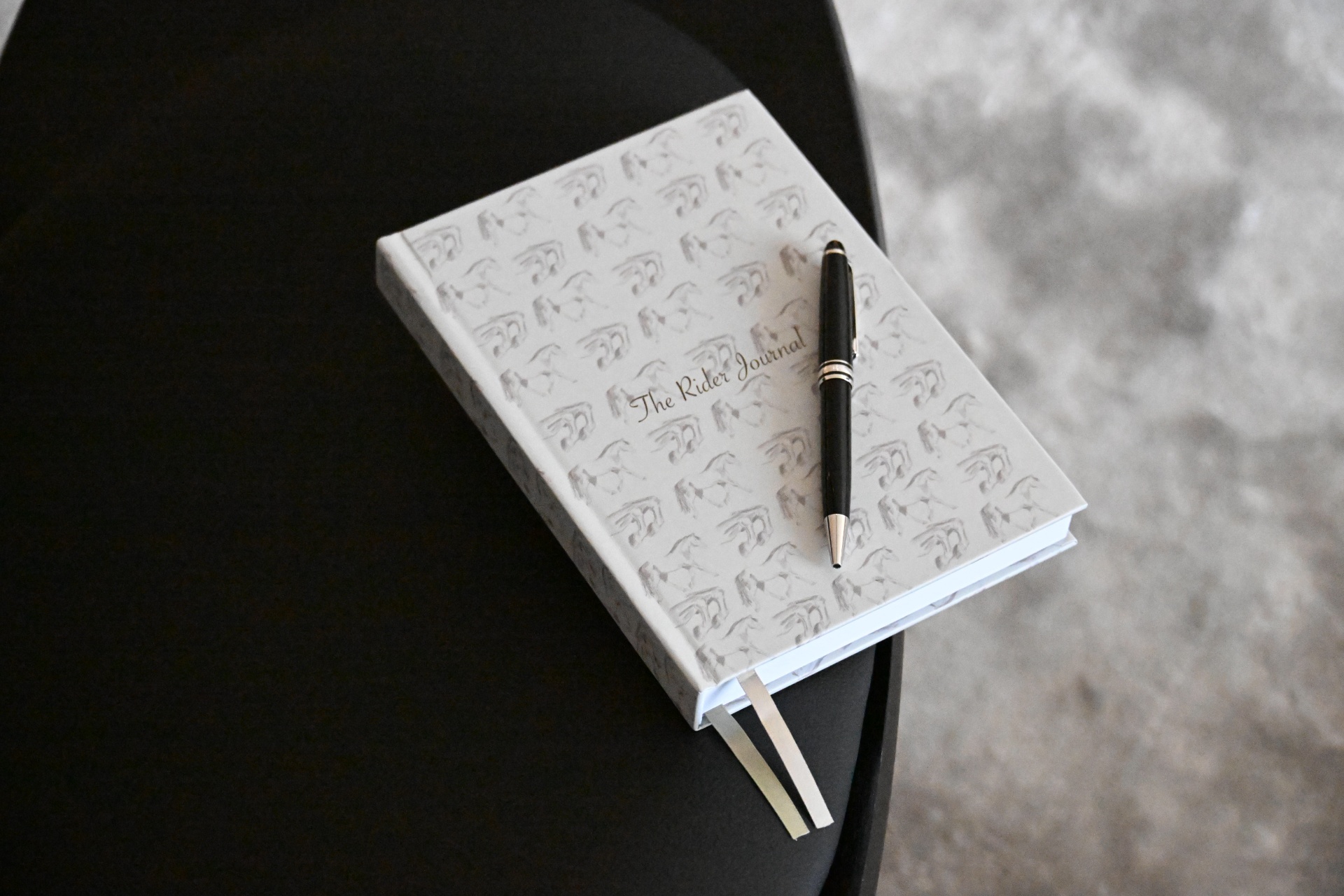 The Rider Journal on a black table with a black and rose gold pen